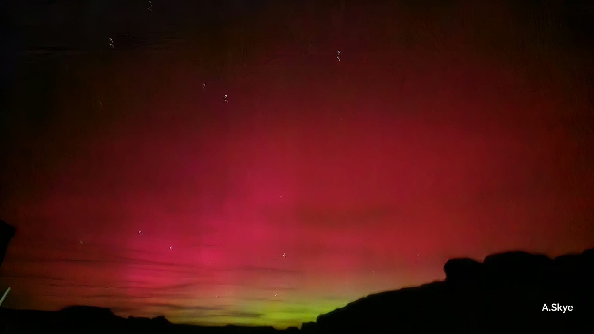 Deep red aurora filling the sky with a band of green low on the horizon, dark rock in silhouette