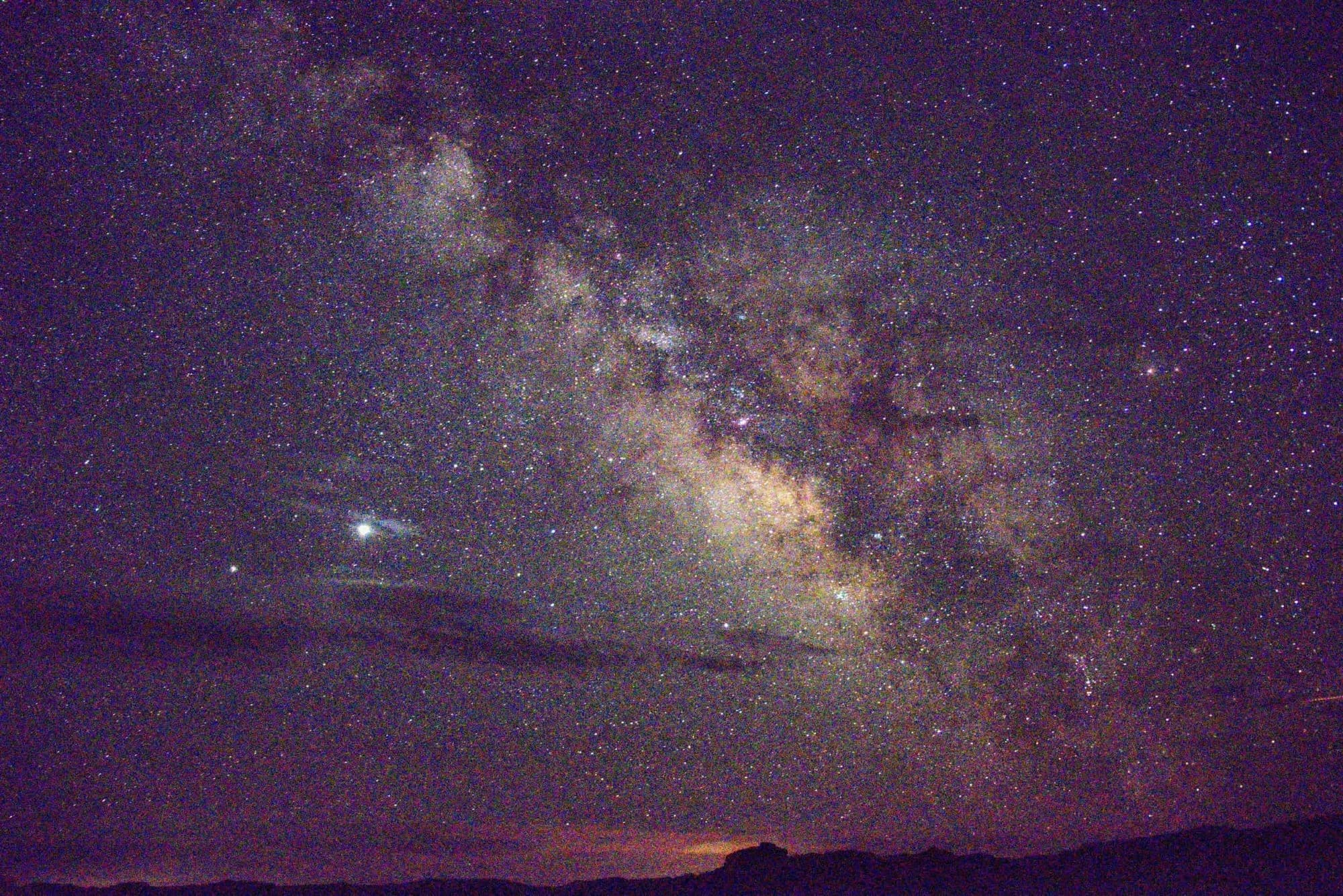 The bright core of the Milky Way over a dark desert ridge, thick with stars